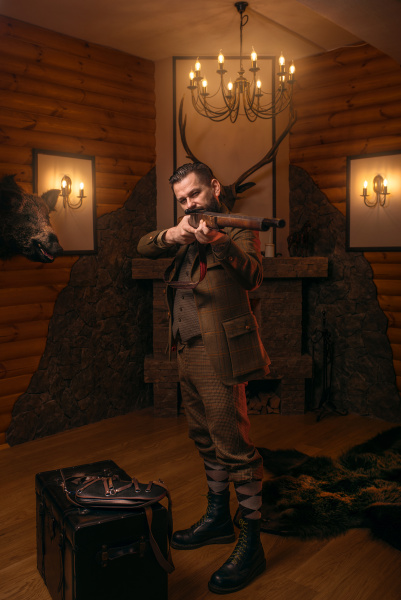 Hombre cazador respetable en ropa de caza con estilo vintage con rifle  antiguo contra chimenea.